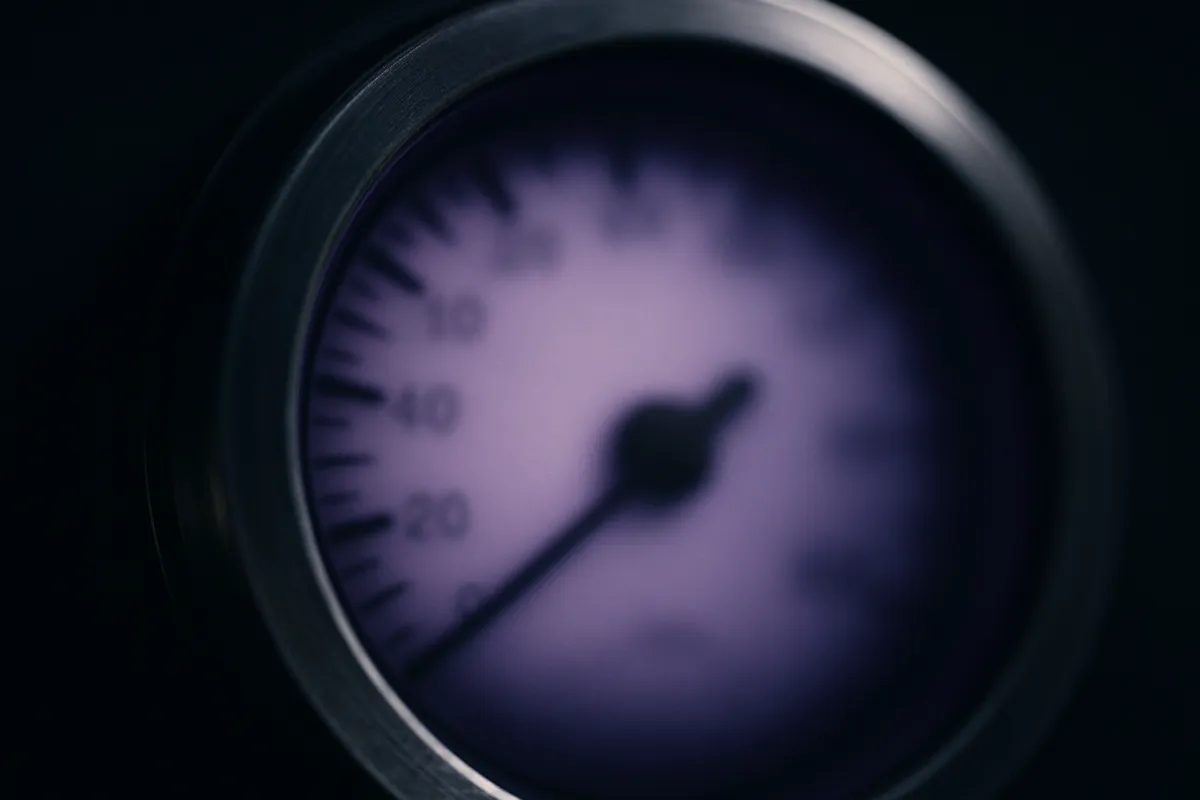 Abstract close-up of a backlit circular dial instrument with a violet glow, needle and markings softly blurred